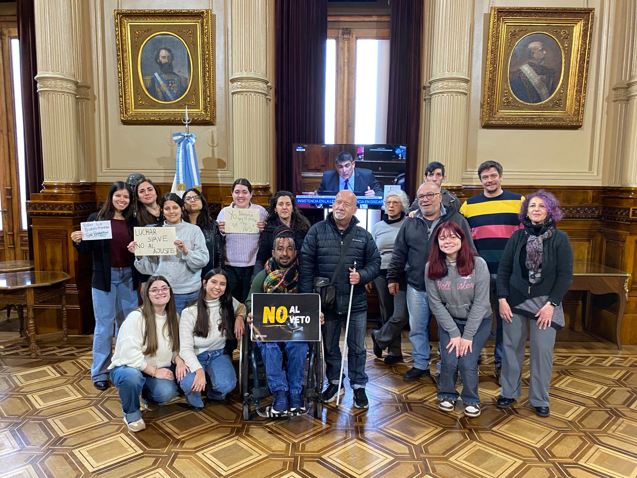 Grupo de personas en un evento, una sostiene un cartel 'NO al veto'
